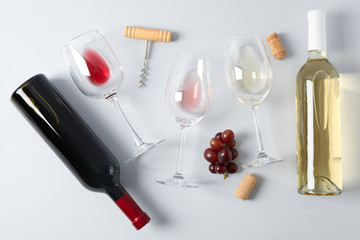 Flat lay. Grapes, corkscrew, bottles and glasses with wine on grey background