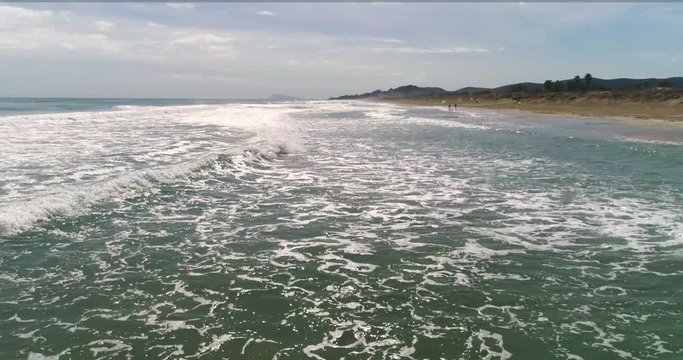 Vuelo rasante de dron sobre las olas de playa dorada mediterr&aacute;neo