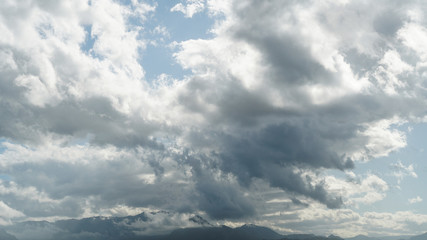 Fototapeta premium Thunderclouds over the tops of the mountains against a clear blue sky in backlight