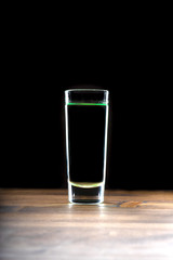 Glass of alcoholic drink on a black background, minimal. Shot of absinthe in a glass on a wooden table.