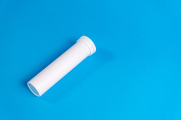 Round white matte aluminum tube with cap for effervescent or carbon tablets, pills, vitamins. Side view. New sealed vertical tube to store medicine lying isolate on blue background. copy space
