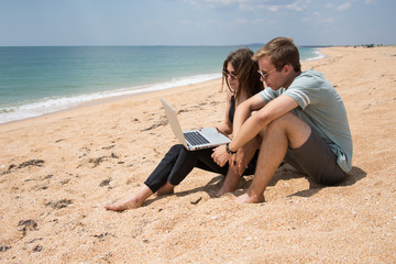 Fototapeta premium Young couple at the sea. Students work on a laptop. 