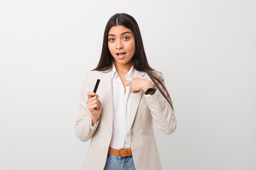 Young arab woman holding a credit card surprised pointing at himself, smiling broadly.