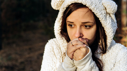 A young woman in a white fluffy hoodie shrinks from the cold in the forest.