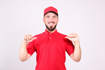 Young handsome delivery guy wearing red uniform and cap holding the blank cardboard box over isolated white background. Portrait of friendly bearded man carrying parcel. Copy space for text.