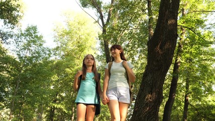 Naklejka na ściany i meble teamwork tourists teenagers. happy girls travelers go with backpacks in forest. Hiker woman walks in the forest. happy hiker girl in summer park. teenager girl adventures on vacation.