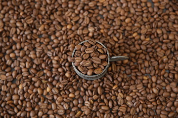 organic coffee grains in a metal cup on the background of roasted aromatic coffee beans. Coffee beans background concept.