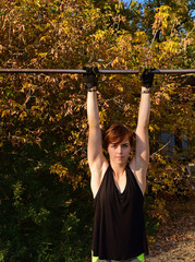 Fototapeta premium Young sporty girl hanging on a sports bar anf background of autumn foliage.
