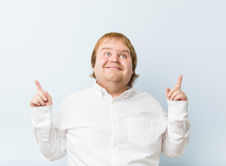Young authentic redhead fat man indicates with both fore fingers up showing a blank space.