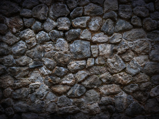 Stone wall of dark rough cobblestone with vignette