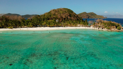 aerial view beach with tourists on tropical island, palm trees and clear blue water. Malcapuya, Philippines, Palawan. Tropical landscape with blue lagoon
