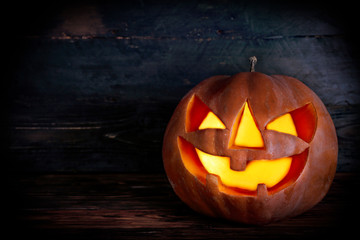 Orange pumpkin carved into creepy and funny Jack o Lantern w/ glowing eyes on dark background. All...