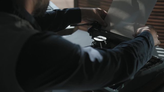Men load paper in the tray of a typewriter and starts typing. The beginning of creativity. Close-up, typewriter, vintage atmosphere. Taken from the back of unknown man,
