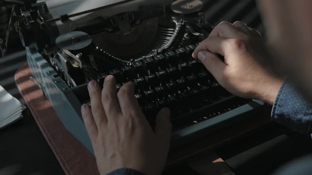 A man is typing a document on a vintage typewriter, shot from above closeup. Sunlight on the desk and male hands. Work at the typewriter, retro style.