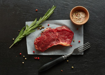 Beef chop steak with rosemary and spices fork on black slate background