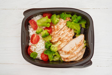 Lunch box. Rice, chicken, tomatoes, cauliflower in a plastic container on a white wooden background. View from above. Flat lay.