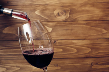 Pouring red wine into a vine glass with decanter or aerator attached to bottle neck. Rustic wooden background. Place for text. Copy-space.