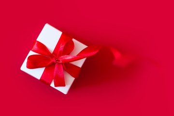 White box with a red ribbon on a red background, top view, copy space. Greeting card concept