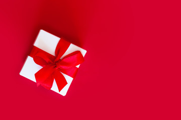 White box with a red ribbon on a red background, top view, copy space. Greeting card concept