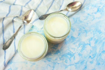 Obraz na płótnie Canvas Greek yogurt in glass jars with spoons on a blue background. Top view. Copy space.