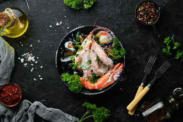 Boiled Seafood in a creamy sauce on a black stone plate. Seafood, prawns, shellfish, lobster. Top view. Free copy space.