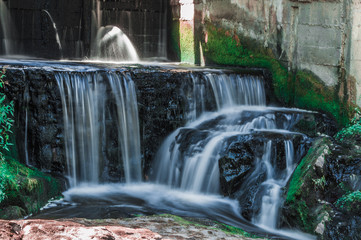 Small waterfall under the dam with rapids and green moss