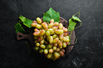 Fresh green grapes with leaves on a black stone table. Top view. Free space for your text.
