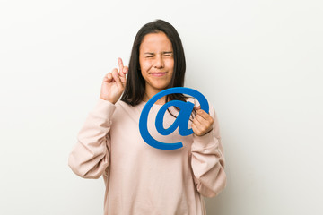 Young hispanic woman holding an at icon crossing fingers for having luck