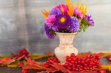Bright autumn purple and yellow flowers in a vase stand on the table in dry red  autumn maple...