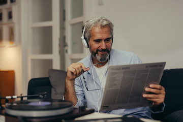 mid aged man relaxed in sofa listening music record player in his home