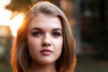 Naklejka premium Closeup portrait of a young attractive girl in backlight against blurred background. Shallow focus. Copyspace.