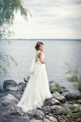 Fototapeta na wymiar The bride in a white dress on the stones near the river