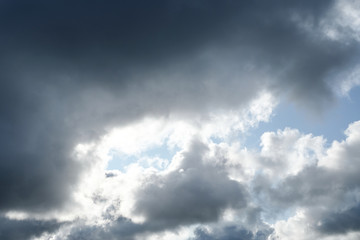 The sun and clouds on the blue sky. Cloudy weather with cumulus, dark clouds. Autumn day. A strong...