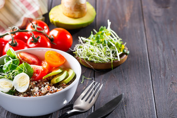 Fresh healthy salad with quinoa, cherry tomatoes and mixed greens, avocado, egg and micro greens on wood background top view. Food and health. Superfood meal. Clean eating. Healthy lifestyle
