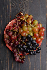 Ripe juicy grapes on a plate on a dark wooden background. Top view.