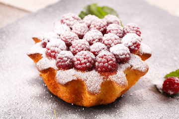 muffin decorated with fresh raspberries on a black plate.