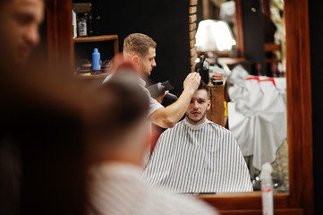 Young bearded man getting haircut by hairdresser while sitting in chair at barbershop. Barber soul.
