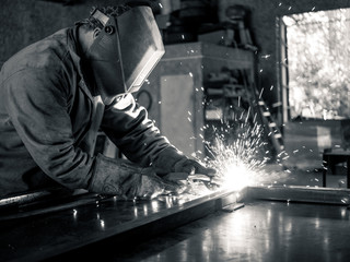 A welder with splatter and a flash reflecting off of his helmet in an industrial setting.