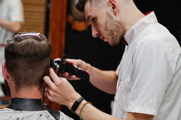 Naklejka premium Young bearded man getting haircut by hairdresser while sitting in chair at barbershop. Barber soul.