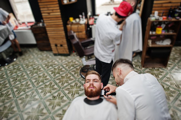 Young bearded man getting haircut by hairdresser while sitting in chair at barbershop. Barber soul.