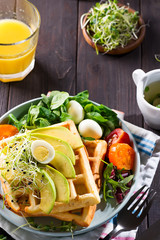 Belgian Waffles with avocado, eggs, micro green and tomatoes with orange juice on wooden table. Perfect breakfast for healthy food or lose weight. Avocado sandwich.