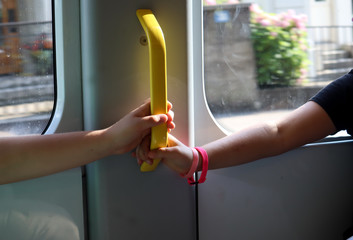 sun lights the hands of a boy and girl  holding a handle on a moving tram, blurred background, safe behavior in traffic, close up