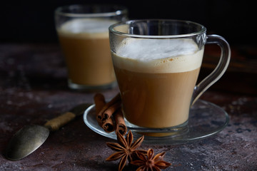 Two cups of hot cappuccino coffee with cinnamon and anise on a brown background