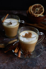 Two cups of hot cappuccino coffee with cinnamon and anise on a brown background