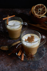 Two cups of hot cappuccino coffee with cinnamon and anise on a brown background