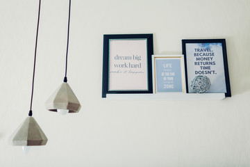 Frames with motivational and inspirational quotes put on shelf by chandeliers. Interior design. Home decor