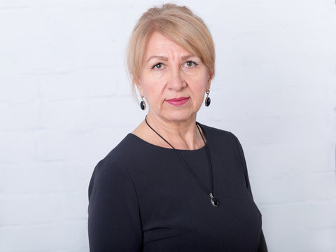 Close Up Portrait Of A Mature Woman In A Black Dress On A Light Background.