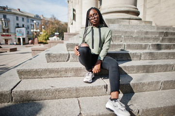 City portrait of positive young dark skinned female wearing green hoody and eyeglasses.