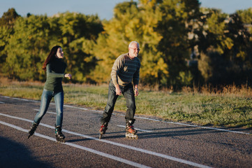 Fototapeta premium Parents and children spend time together. Older generation and sport. Active lifestyle of the pensioner. Happy old man riding on rollers with his daughter on the road in autumn park.