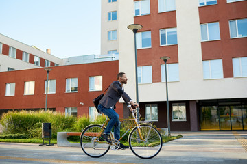 Bearded Businessman in business suit riding on retro bicycle to work on urban street in the morning on sunset